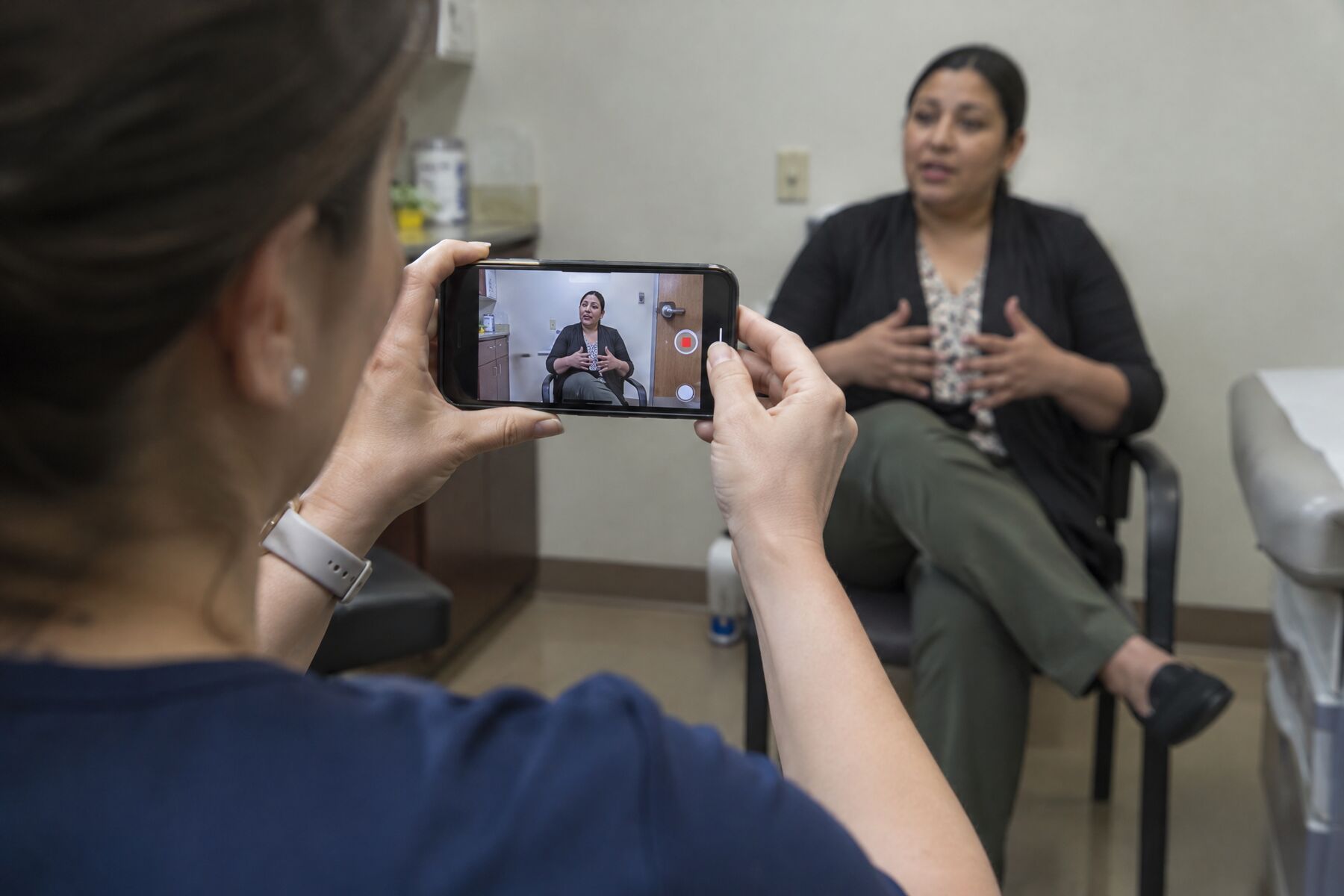 A team member filming a patient on a phone in a consult room